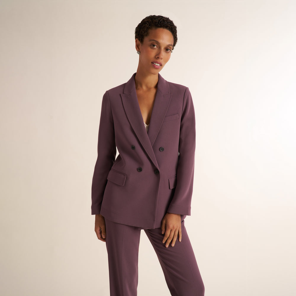 A model wearing a matching mauve double-breasted blazer and trousers set, photographed against a plain light beige studio background.