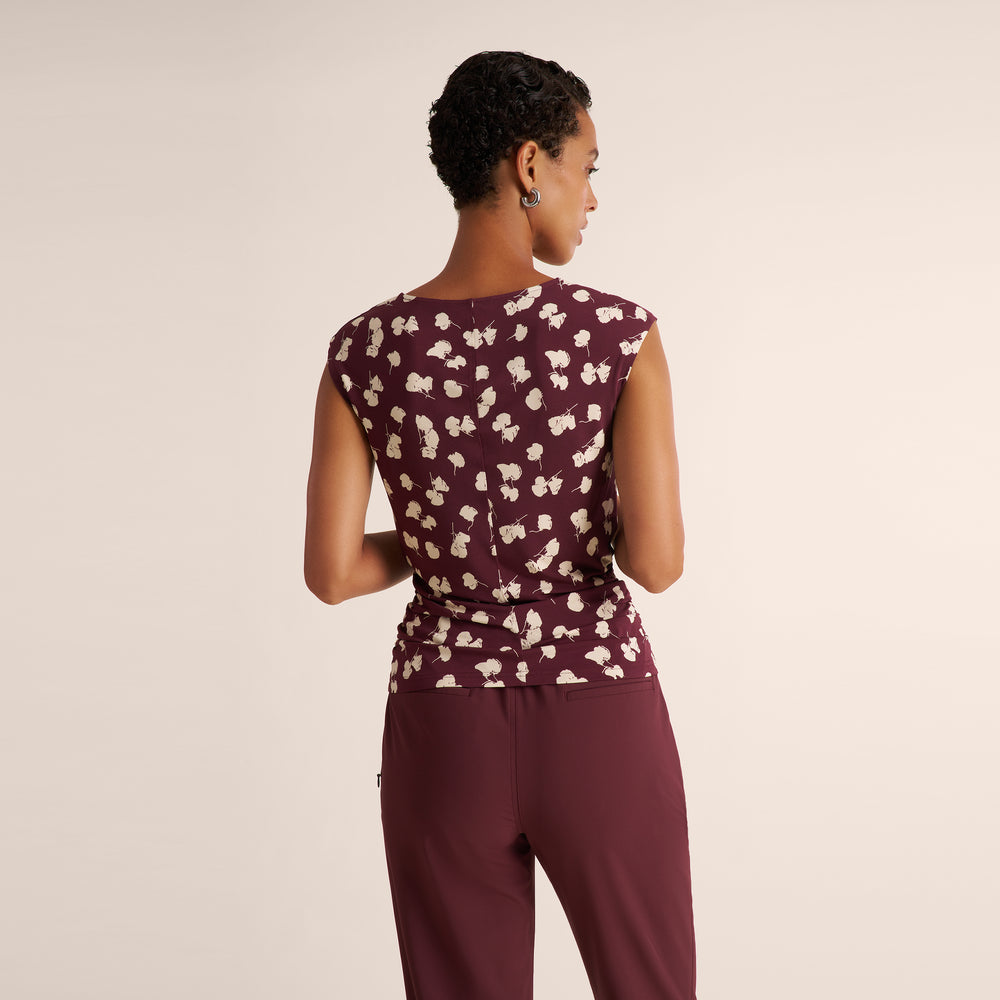 A woman shown from the back wearing a sleeveless burgundy top with a cream floral pattern and matching burgundy pants, photographed against a plain light beige studio background.