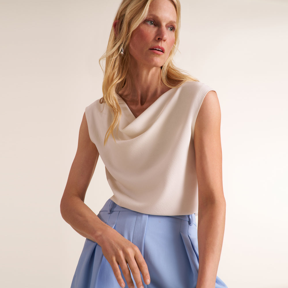 Woman wearing a cowl neck sleeveless top with light blue pants