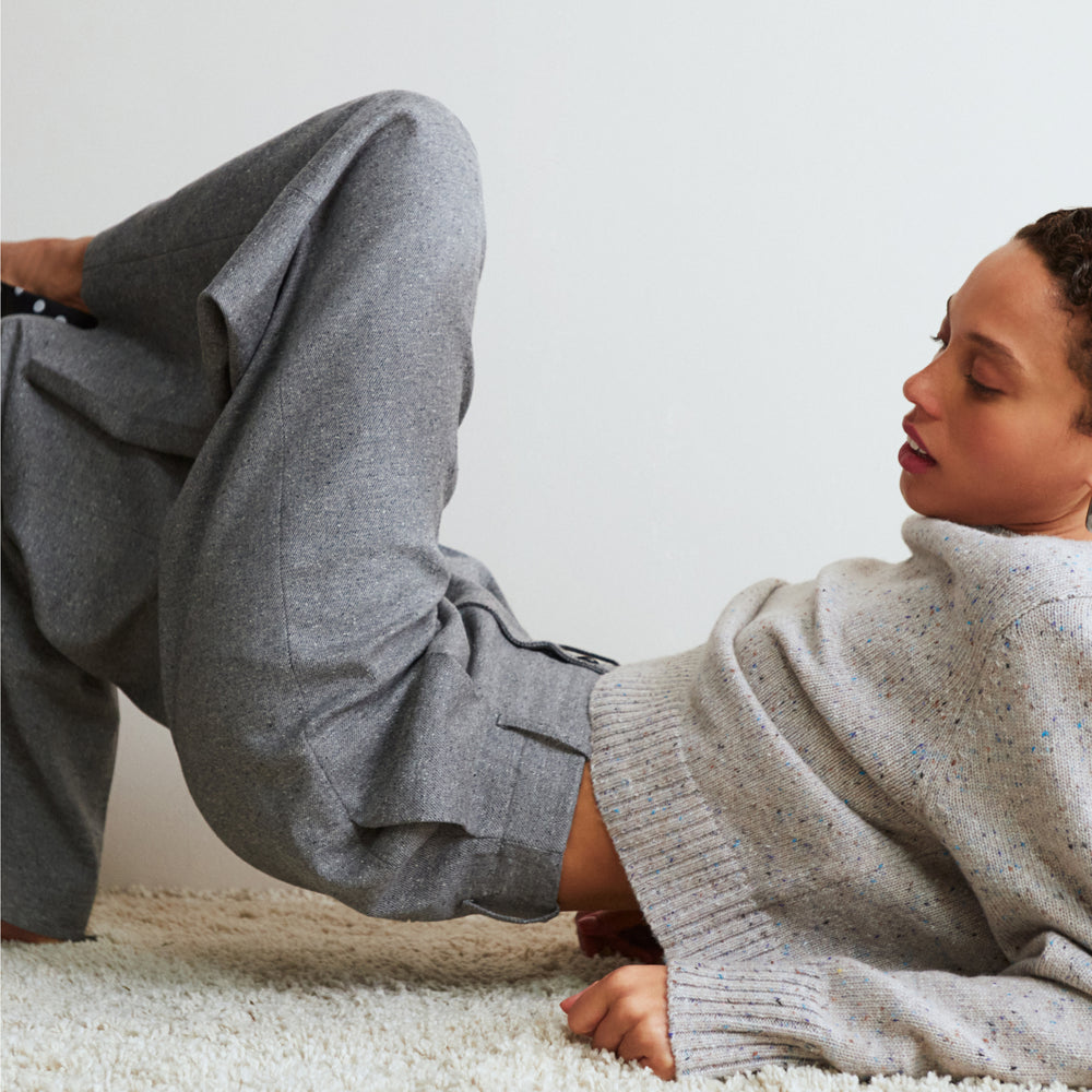 Person lying on a carpeted floor wearing gray pants and a beige sweater.