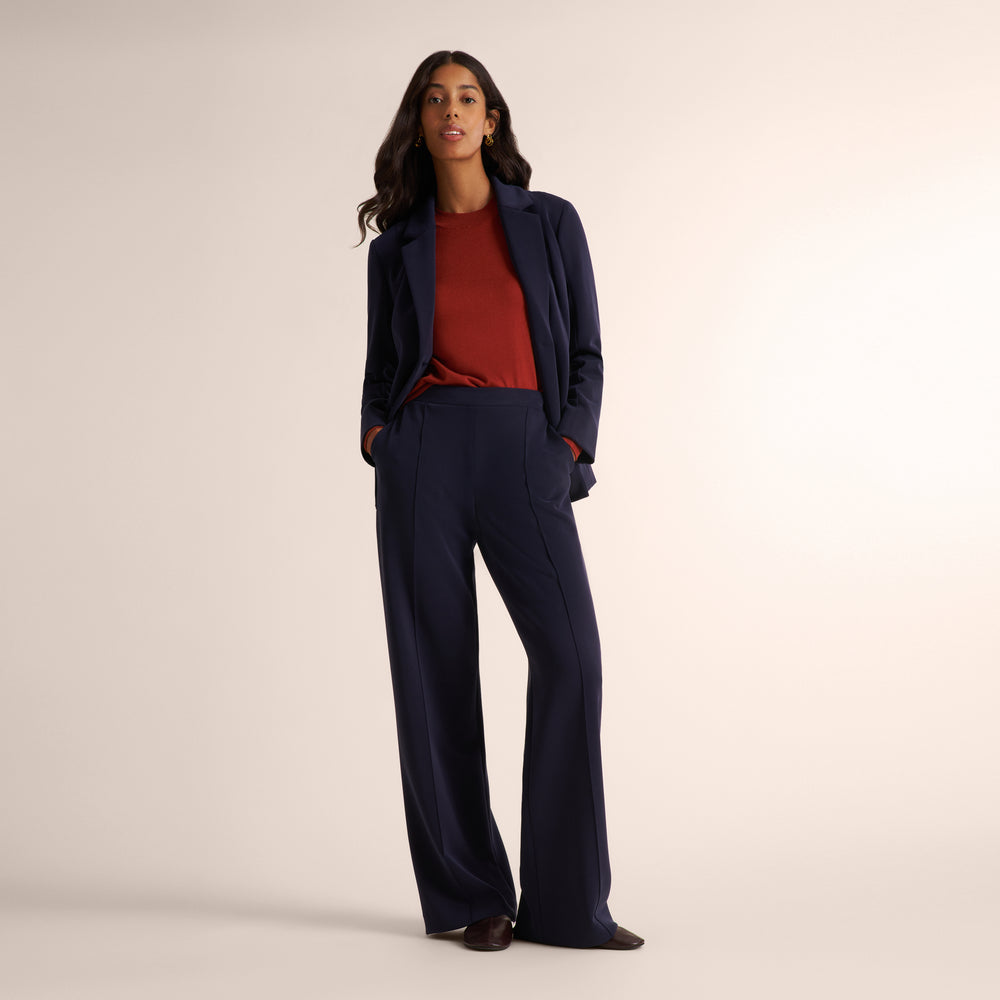 Woman wearing a orange spice color long sleeve sweater with a matching navy suit