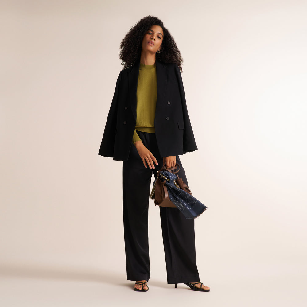 Woman wearing a black double breasted blazer with matching wide leg pants and an olive green long sleeve sweater