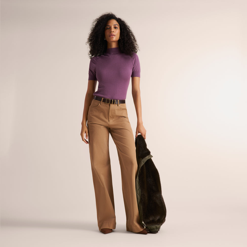 Woman wearing wide leg saddle colored pants, a turtleneck short sleeve in fig purple, and a brown belt.