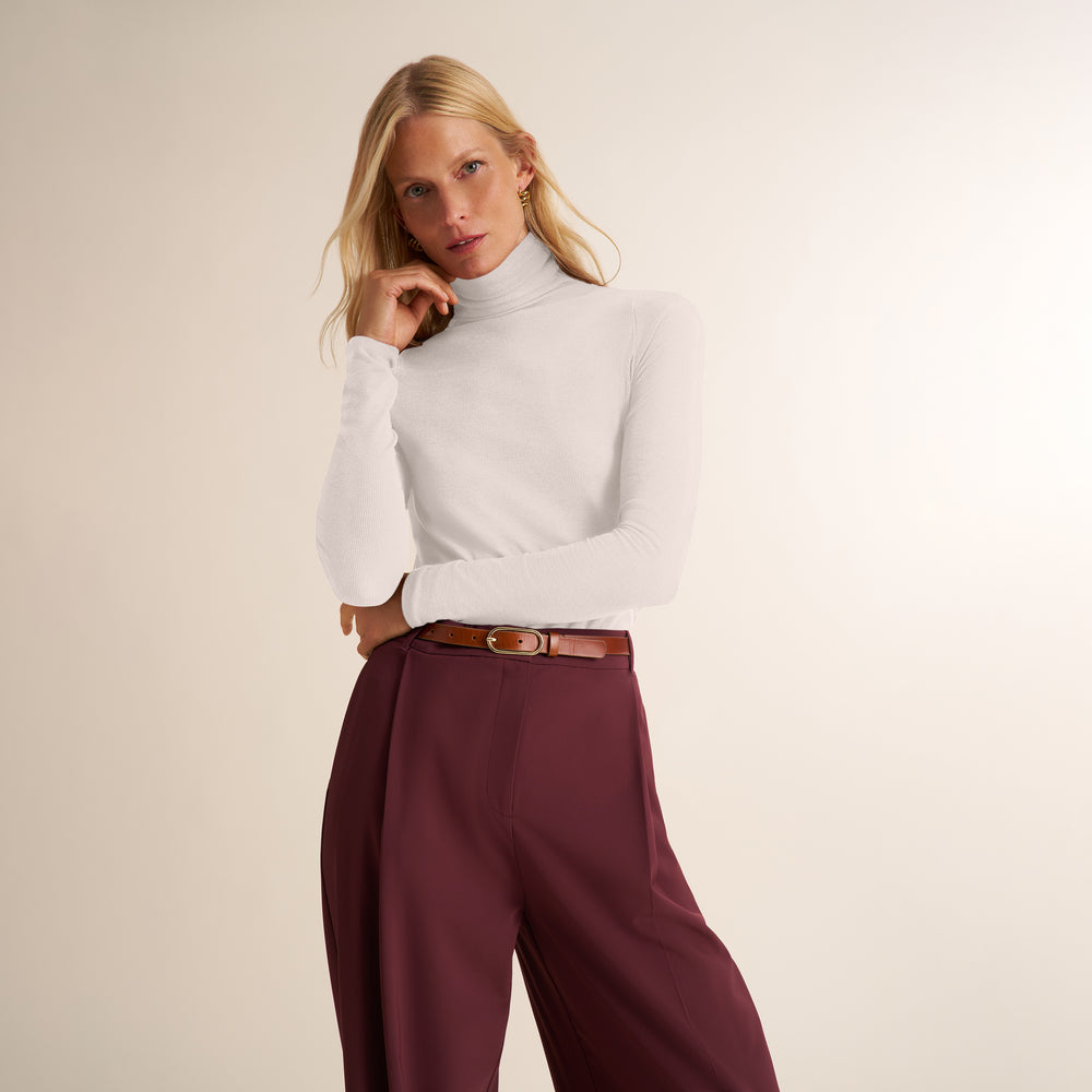 Woman wearing a long sleeve, white ribbed turtleneck with aubergine pants