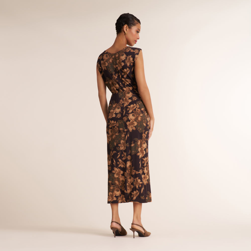 A woman is shown from the back wearing a sleeveless midi dress with a brown and black floral pattern, paired with brown high heels, against a plain beige studio background.