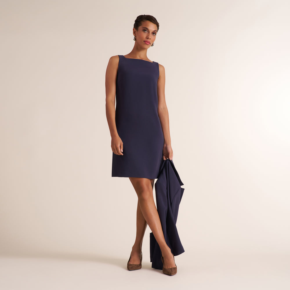 Woman wearing a gray navy square neck sleeveless shift dress with matching blazer in her hand