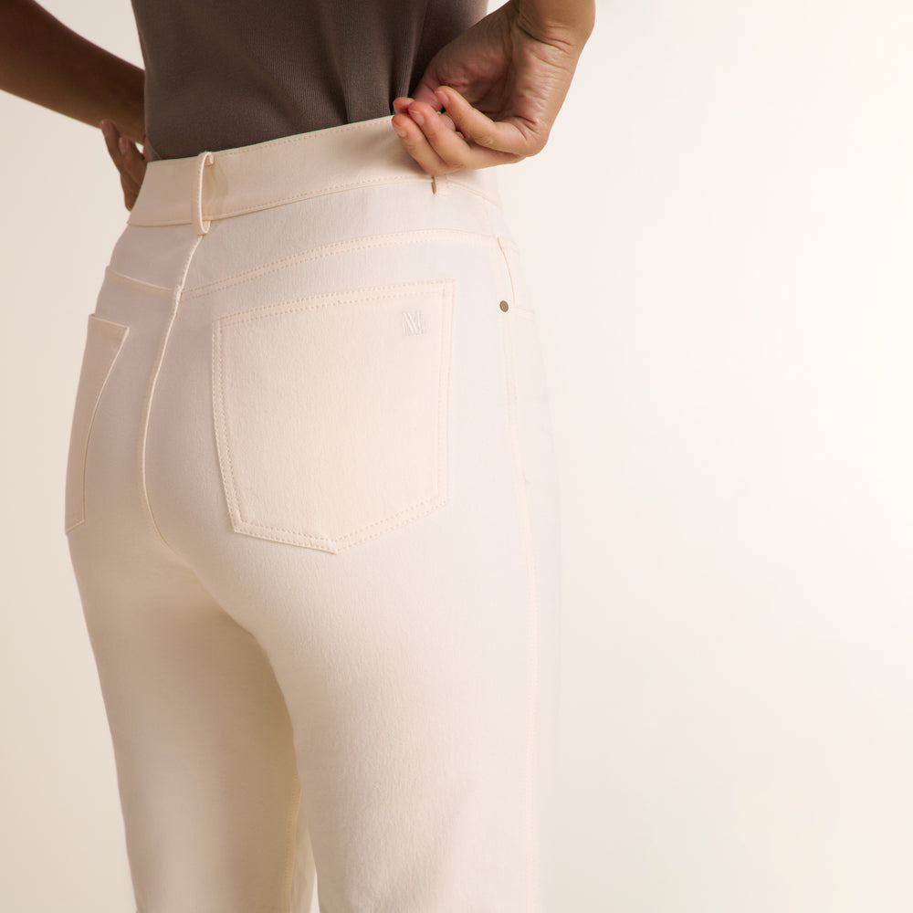 Close-up back view of a person wearing cream-colored high-waisted jeans, showing the waistband, belt loops, and back pocket details against a plain light background.