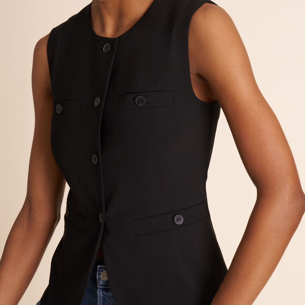 Black sleeveless vest worn by a person on a beige background
