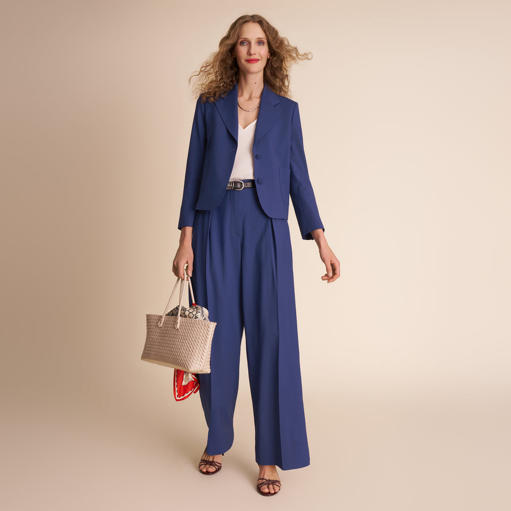 Woman in a blue suit holding a woven bag on a beige background.