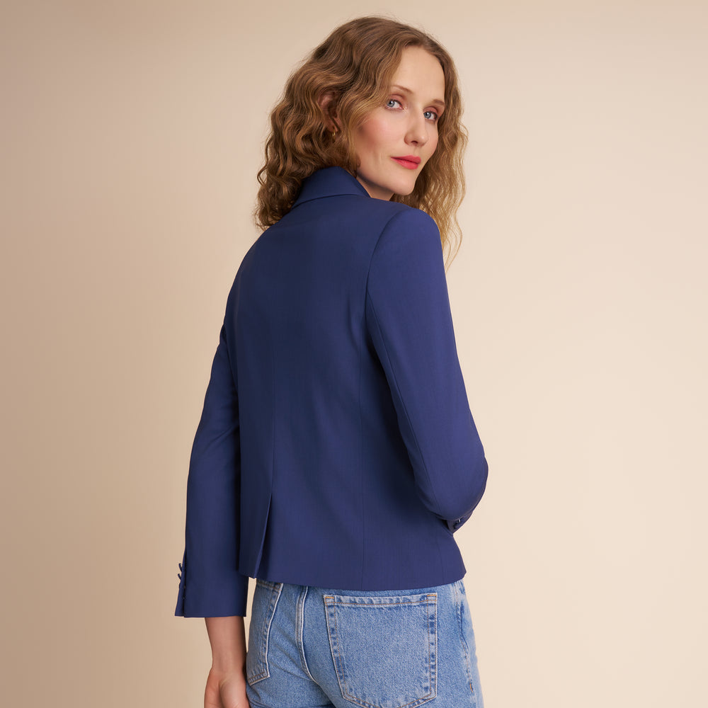 Woman wearing a blue blazer and jeans against a beige background.