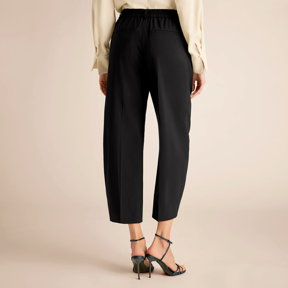 Person wearing black pants and a beige top on a beige background