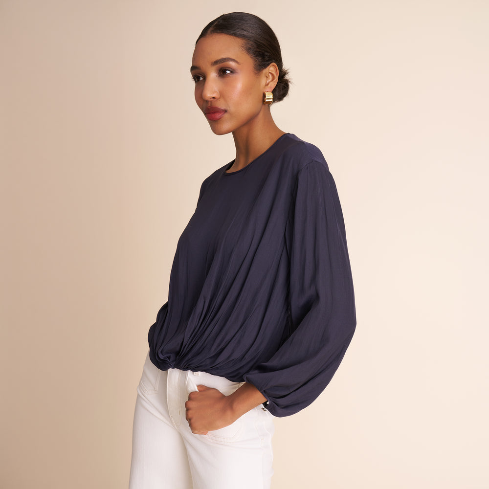 Woman wearing a navy blue top with wide sleeves on a beige background