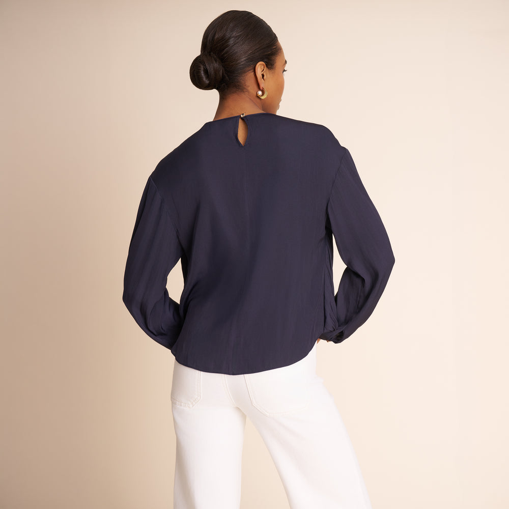 Woman wearing a navy blue blouse and white pants on a beige background