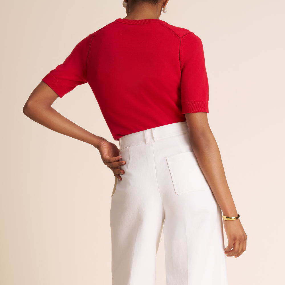 Person wearing a red top and white pants on a beige background