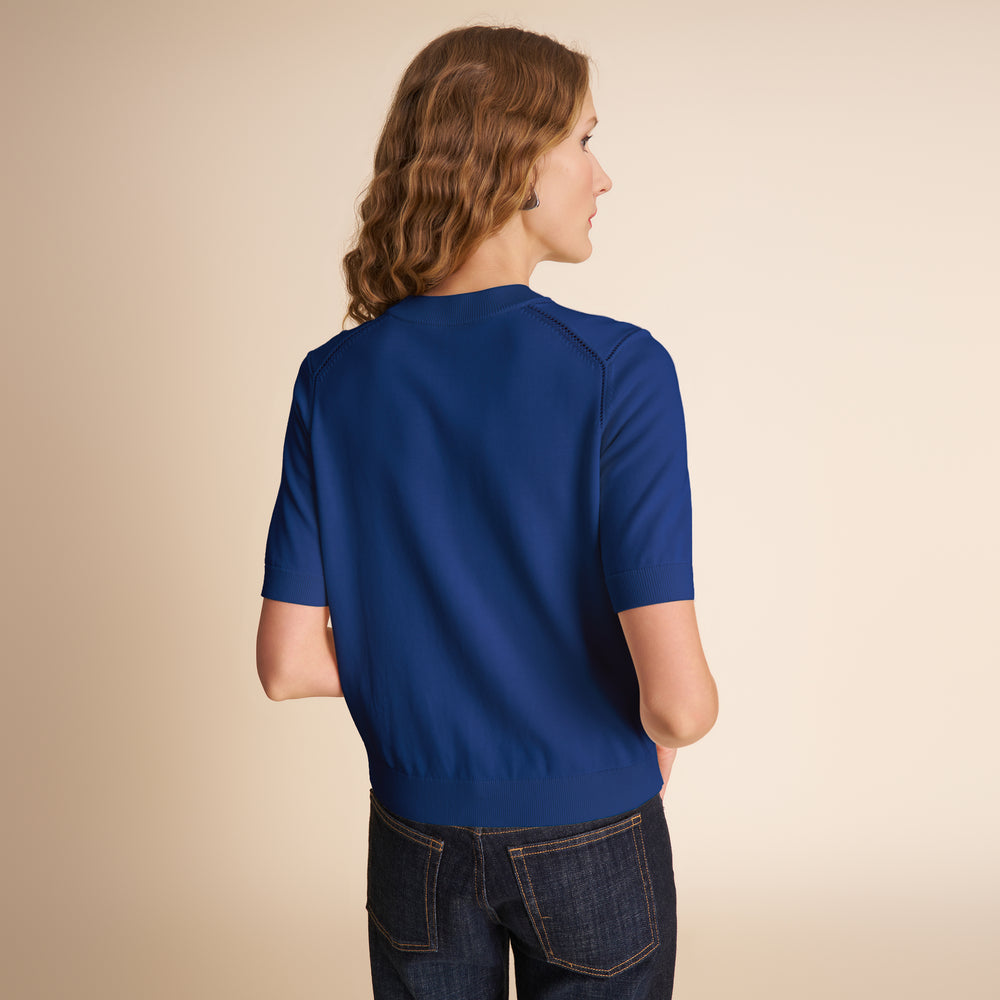Person wearing a blue shirt and dark jeans on a beige background