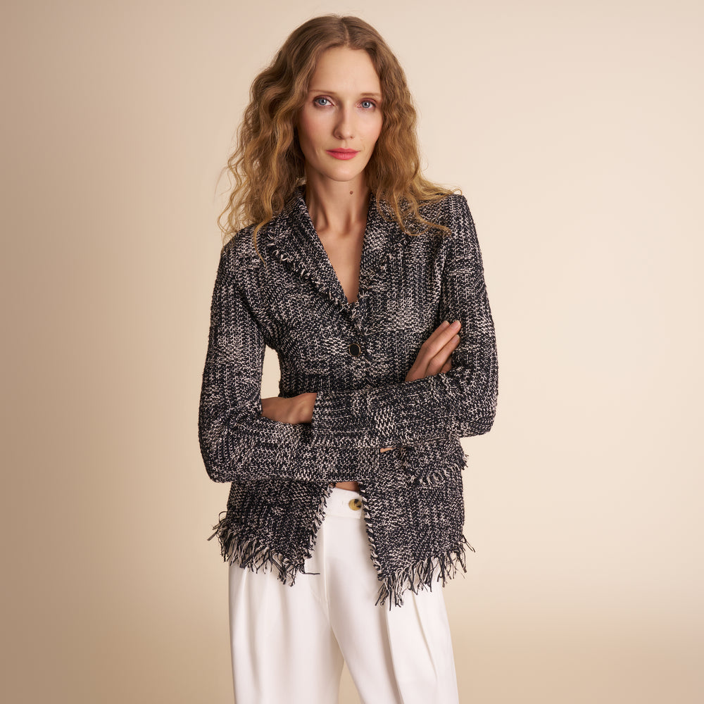 Woman wearing a black and gray patterned cardigan with white pants on a beige background