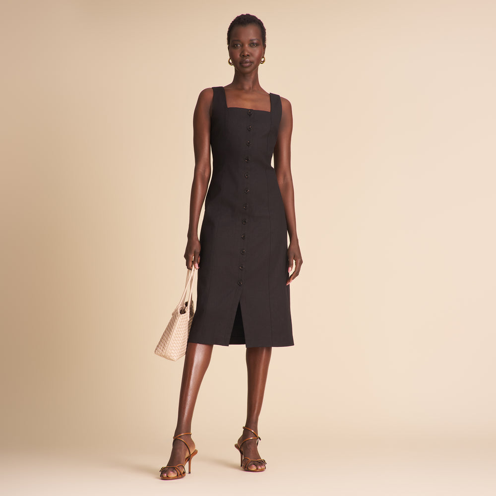 Woman wearing a black linen dress with black buttons on a beige background