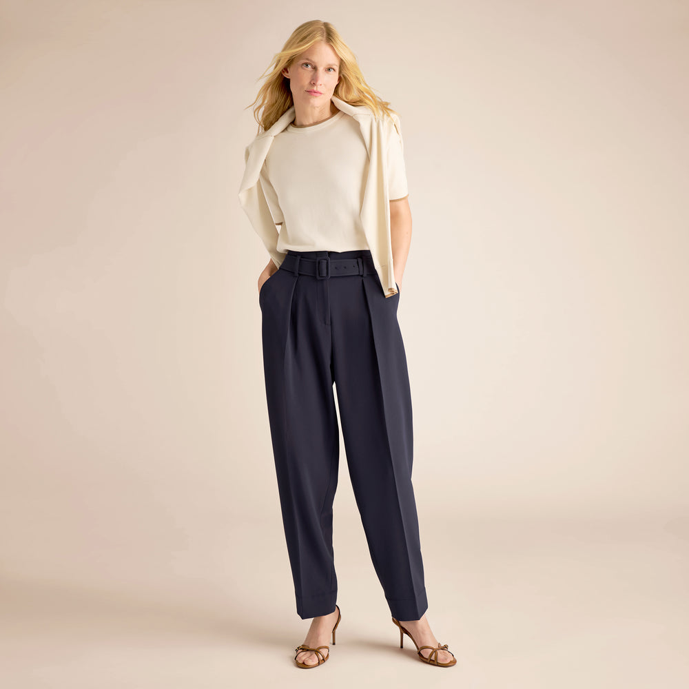 Woman wearing a white top, beige cardigan, and navy pants on a beige background