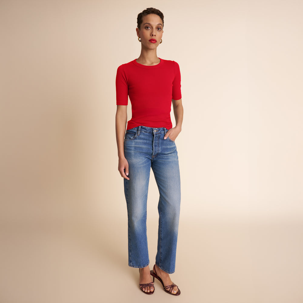 Woman wearing a red top and blue jeans on a beige background