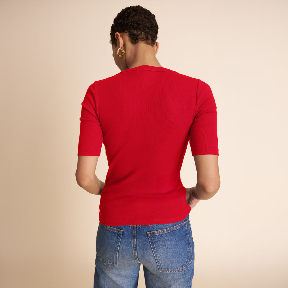 Person wearing a red shirt and blue jeans on a beige background