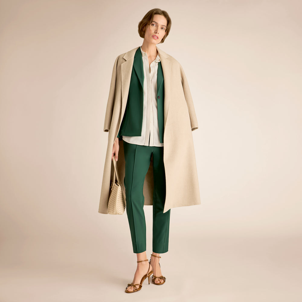 Woman wearing a beige coat over a green outfit on a beige background