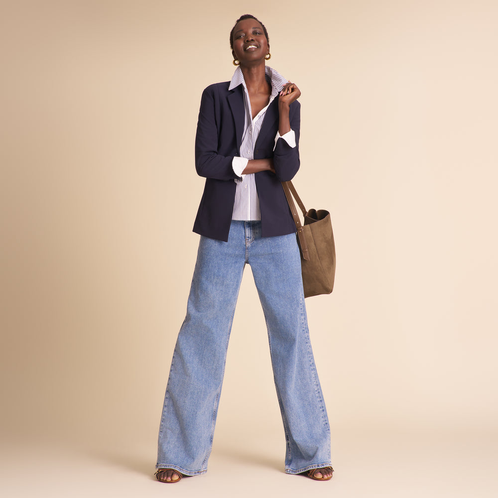 Woman in navy blazer with matching pants and striped shirt sitting against a beige background