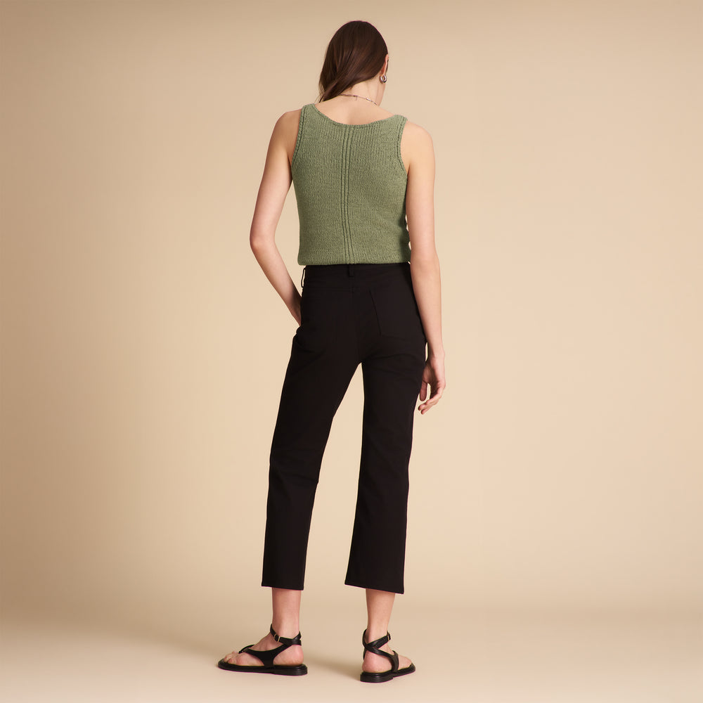 Woman wearing a green tank top and black pants on a beige background