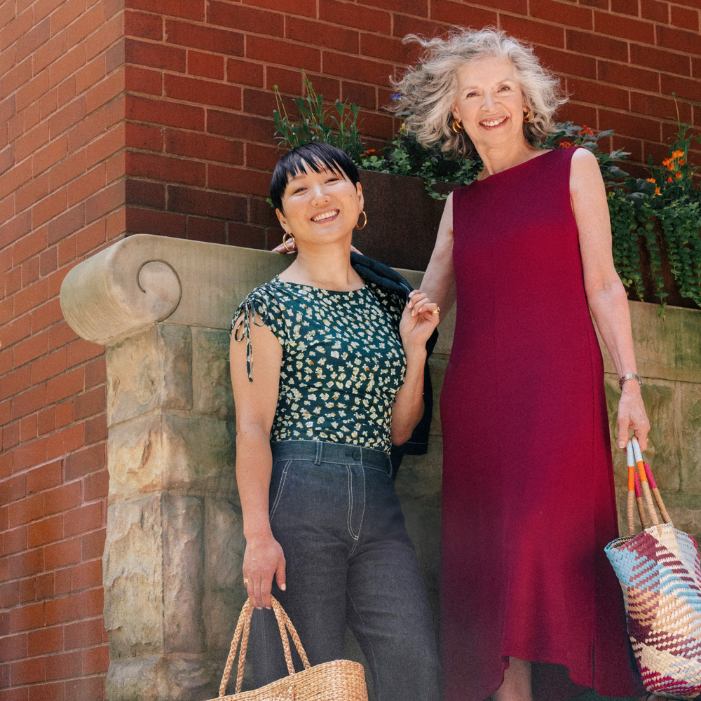 Two women standing together outdoors against a brick wall