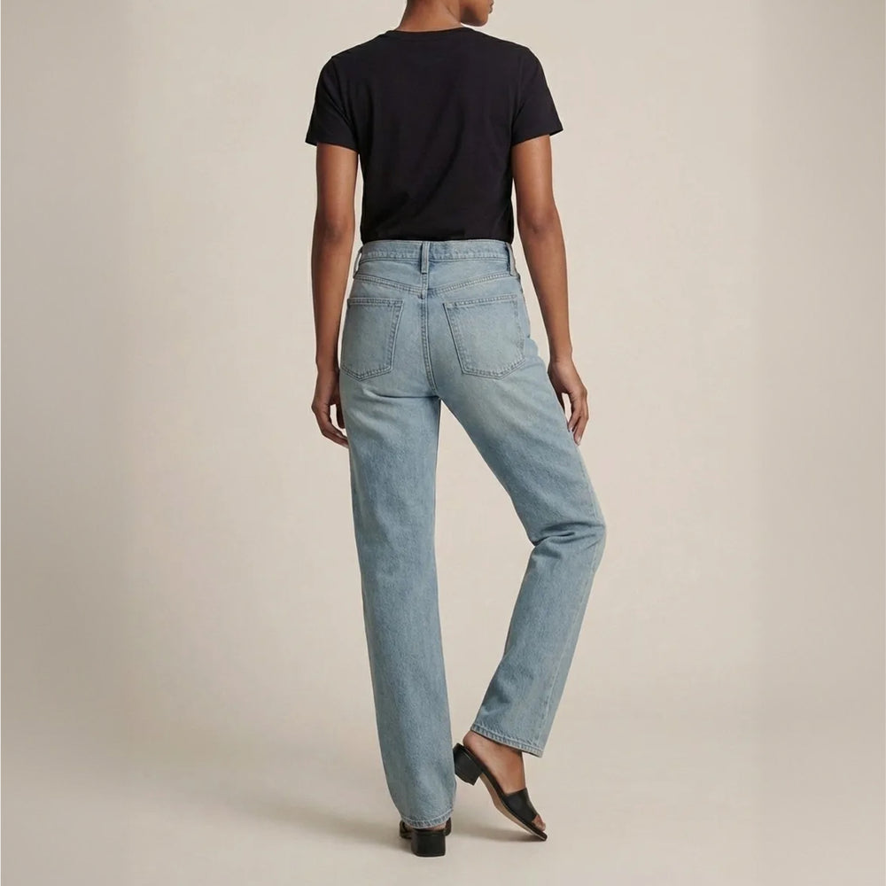 Person wearing light blue jeans and a black t-shirt on a beige background