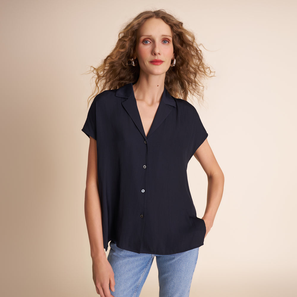 Woman wearing a dark navy short-sleeve blouse with a beige background