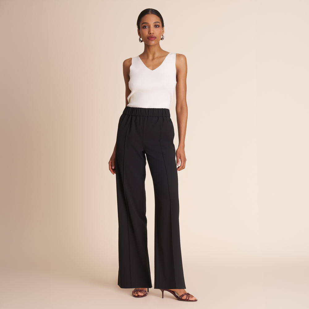 Woman wearing a white sleeveless top and black high-waisted pants on a beige background