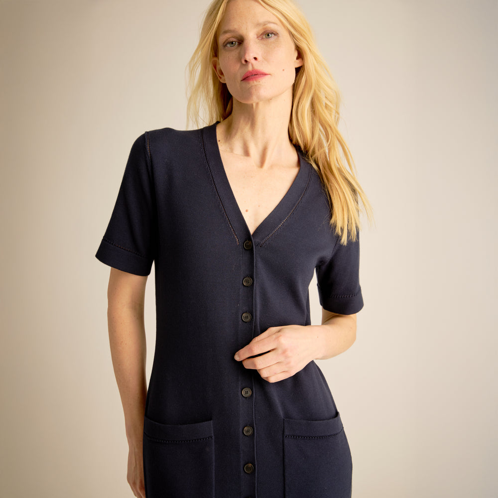 Woman wearing a navy blue cardigan with buttons on a beige background