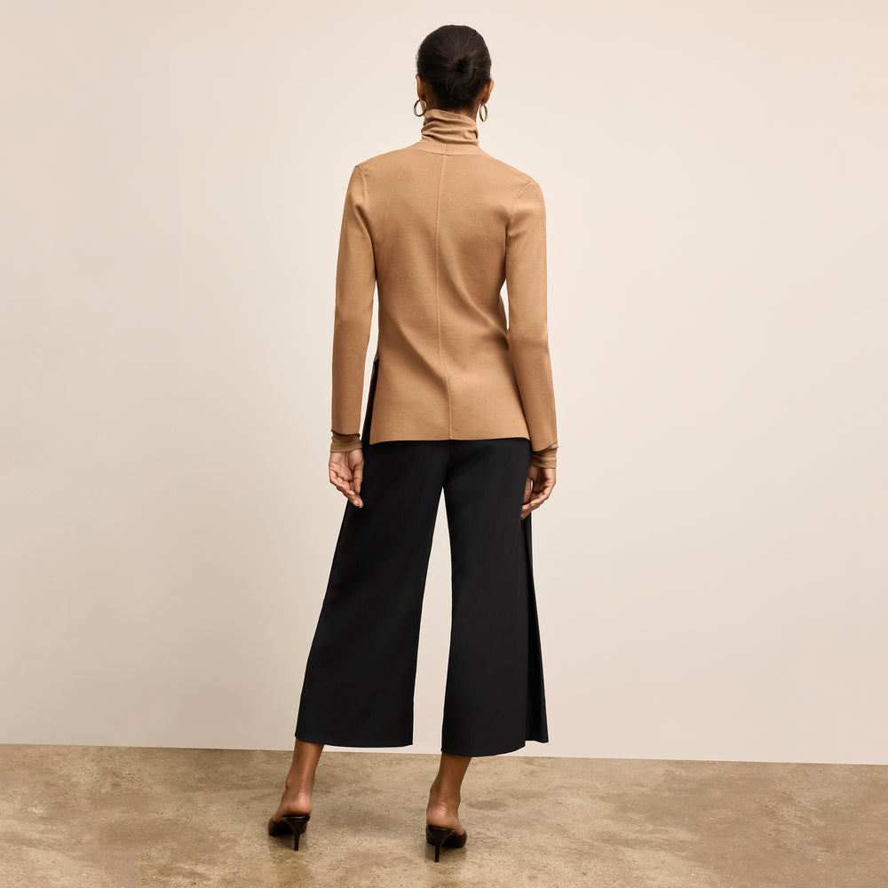 Woman wearing a beige jacket and black pants on a plain background