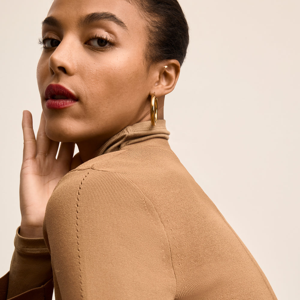 Woman wearing a brown turtleneck sweater against a beige background