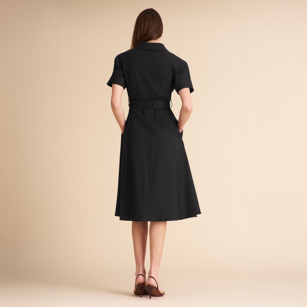 Woman wearing a black dress with a belt against a beige background