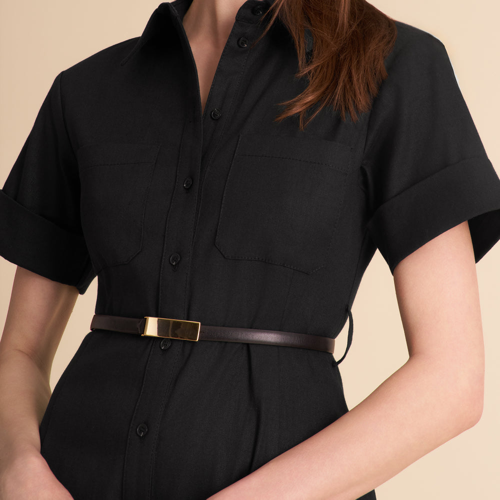 Woman wearing a black dress with a belt against a beige background