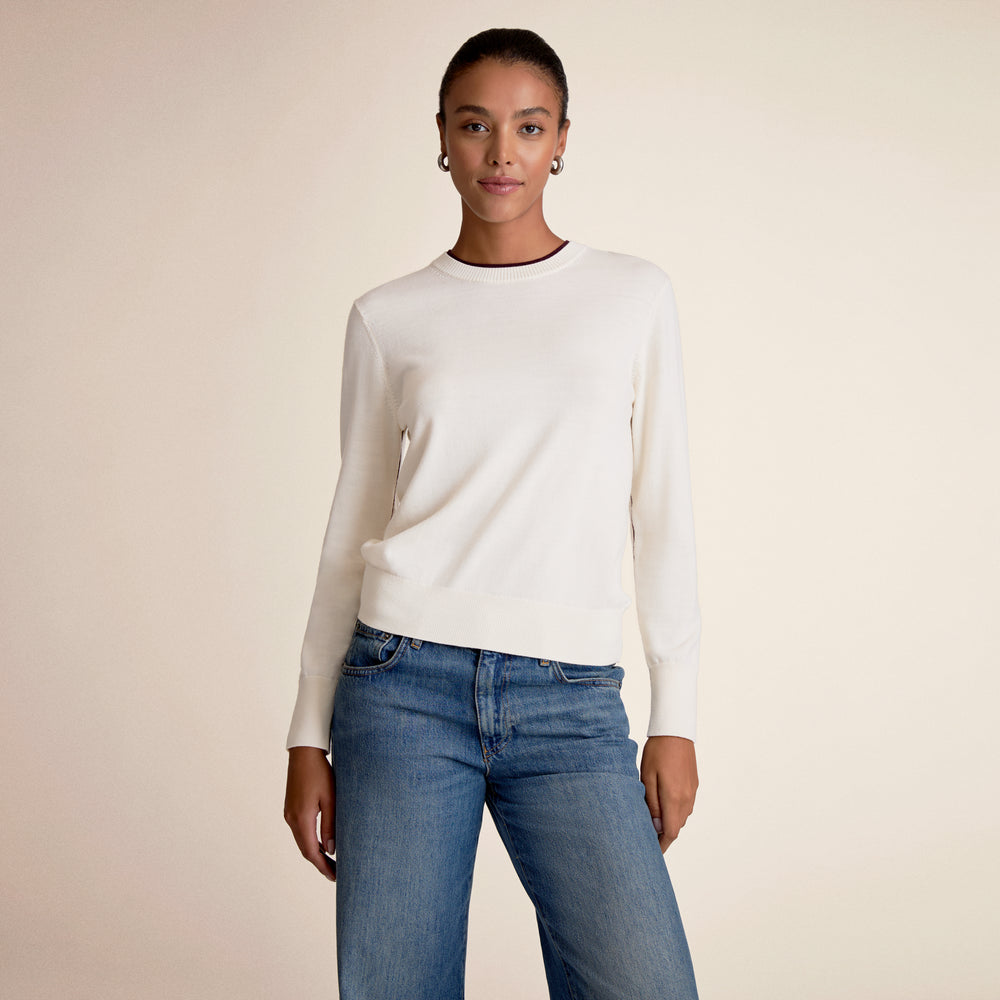 Woman wearing a white sweater and blue jeans against a beige background