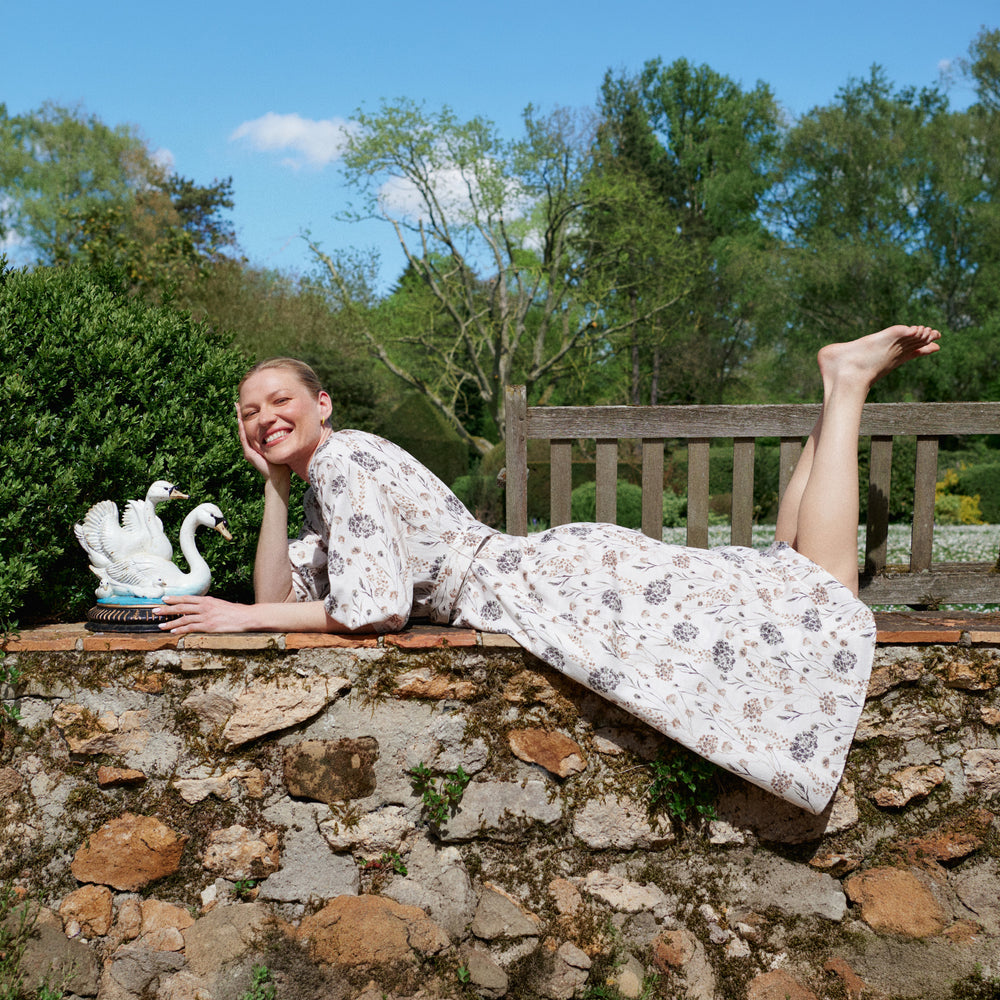 Woman in a floral dress sitting on a stone wall with a garden background