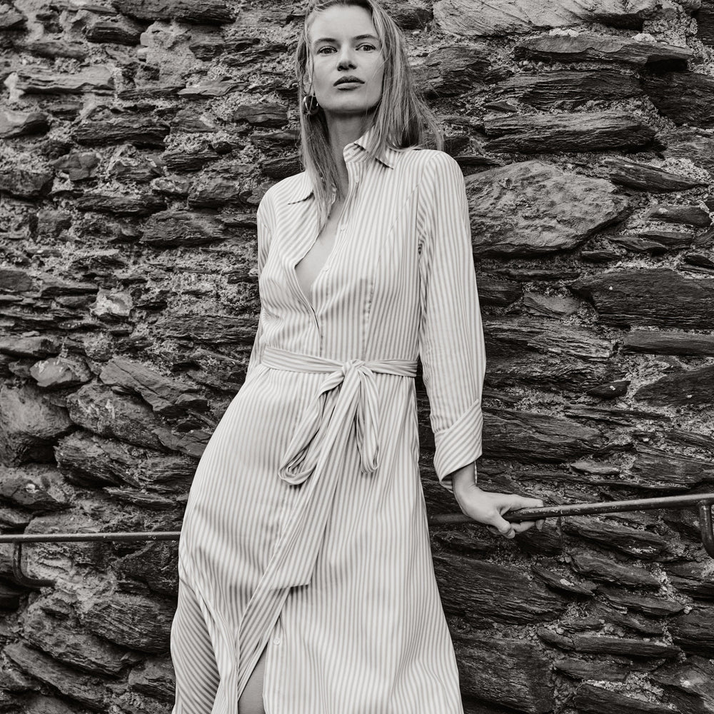Woman in a striped dress standing against a stone wall
