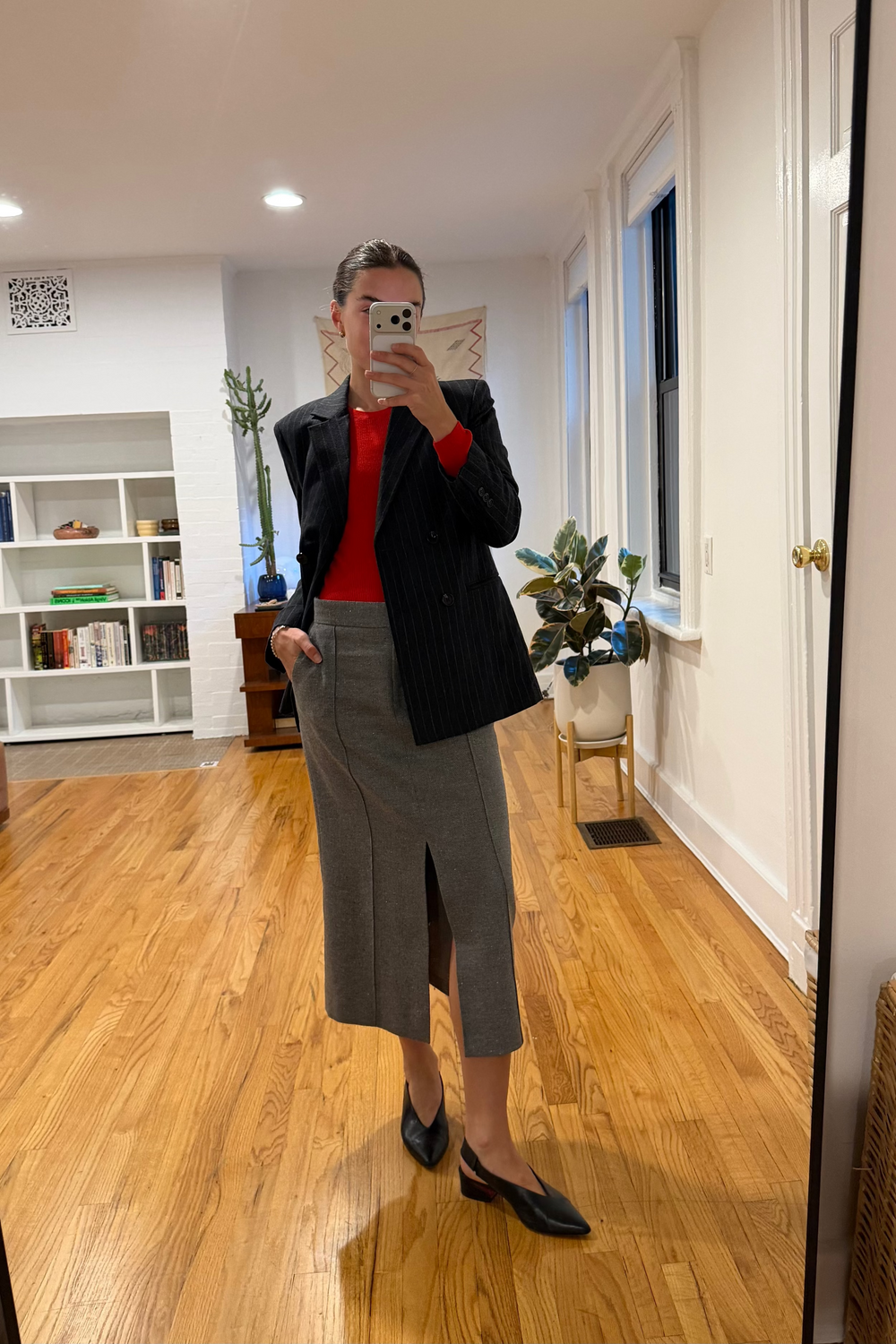 Person taking a mirror selfie in a room with wooden flooring and white walls.