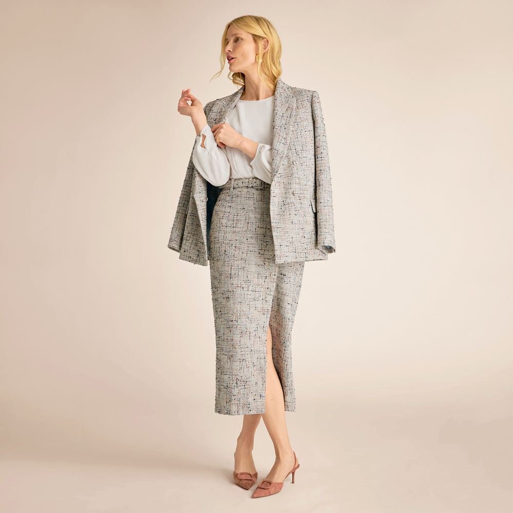 Woman wearing a gray patterned suit with a white shirt on a beige background