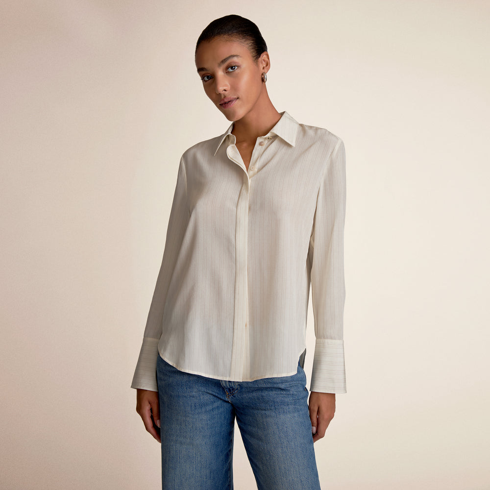 Woman wearing a light-colored shirt and blue jeans against a beige background