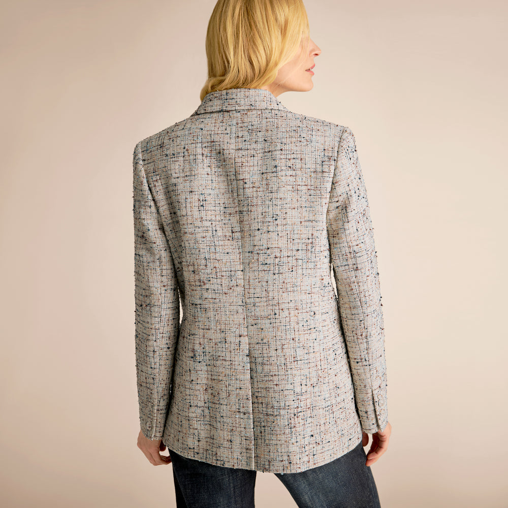 Woman wearing a gray blazer, pink top, and blue jeans on a beige background