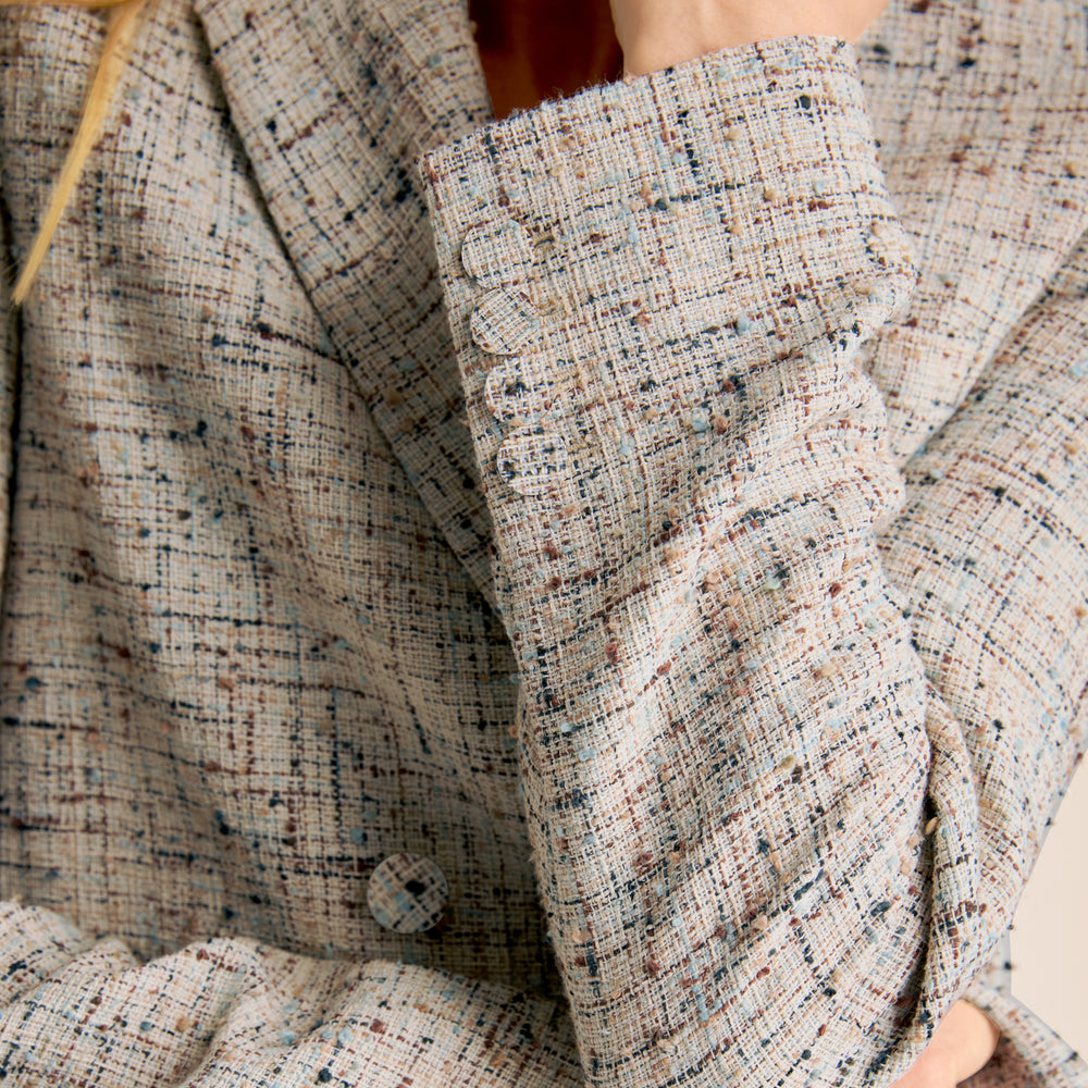Woman wearing a gray blazer, pink top, and blue jeans on a beige background