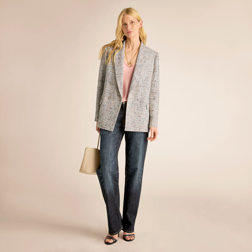 Woman wearing a gray blazer, pink top, and blue jeans on a beige background