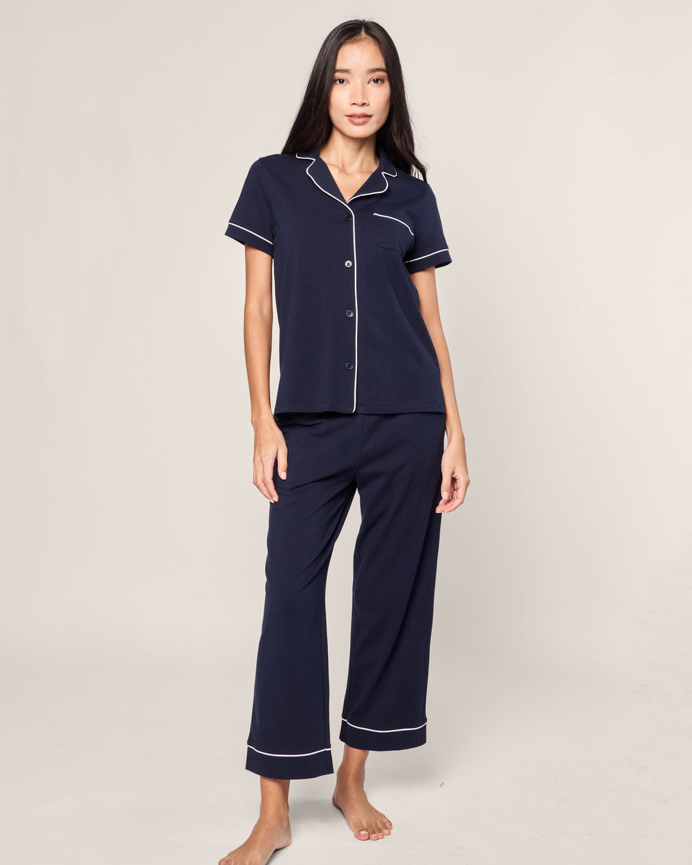 Woman wearing navy pajamas with white piping on a plain background