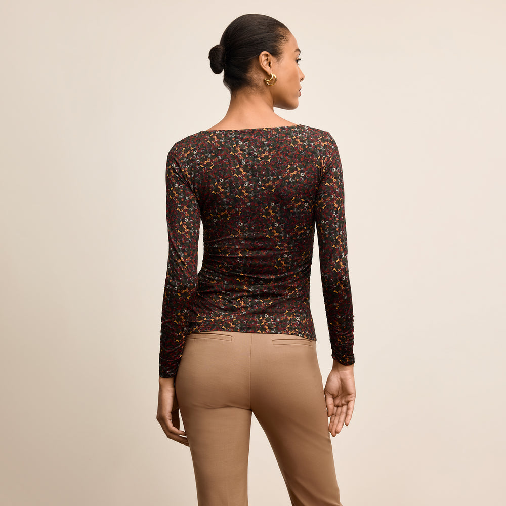 Woman wearing a patterned long-sleeve top and beige pants on a beige background
