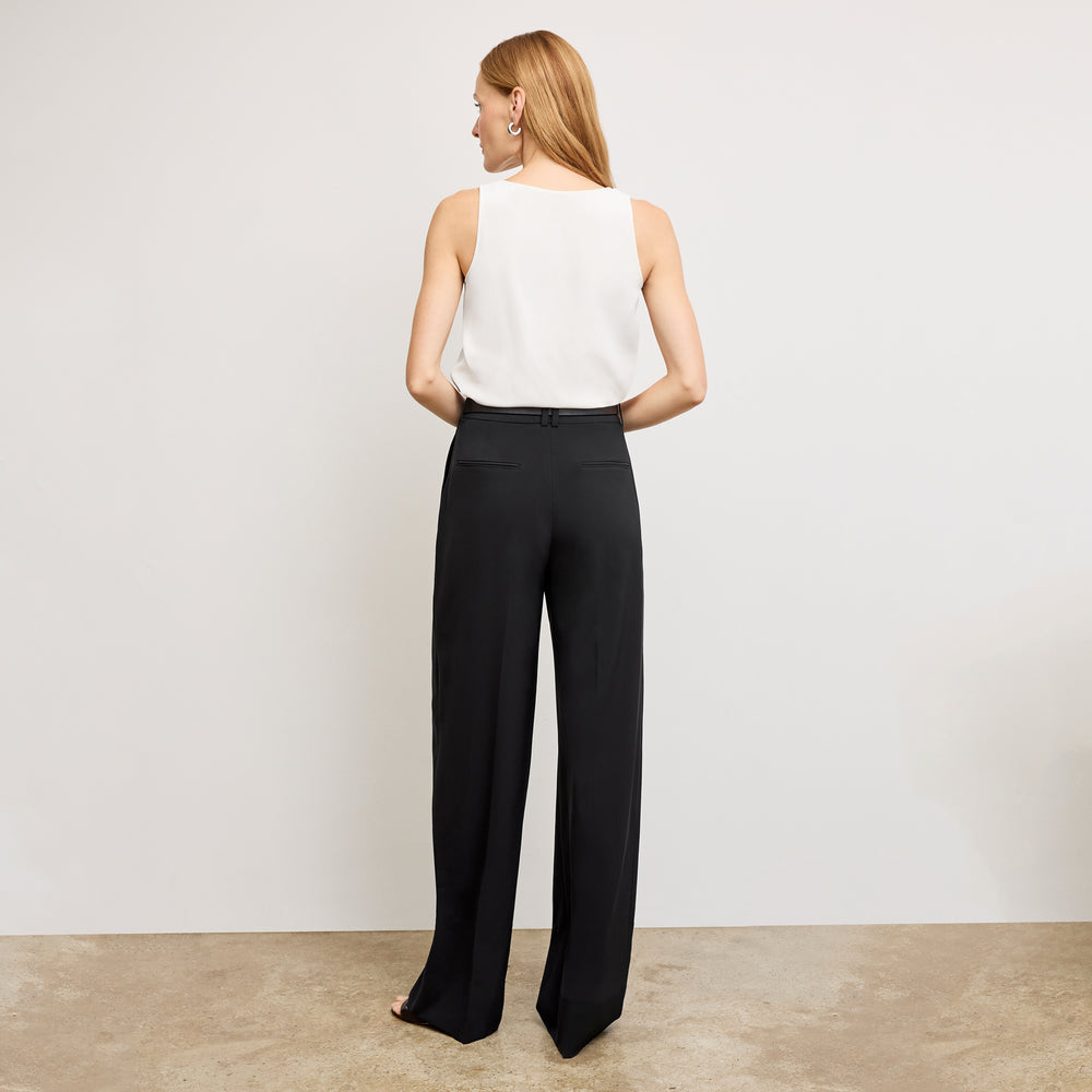 Woman wearing a white sleeveless top and black high-waisted pants against a plain background