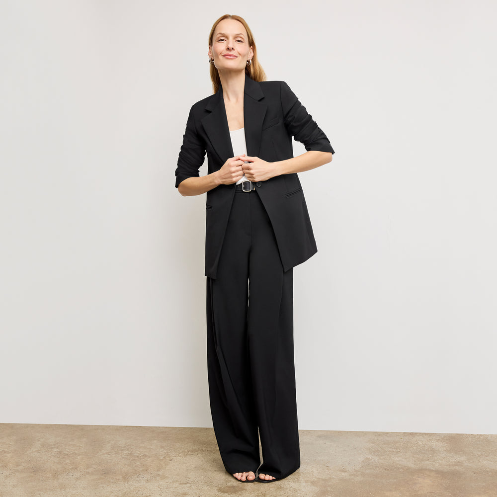 Woman wearing a black suit standing against a plain background