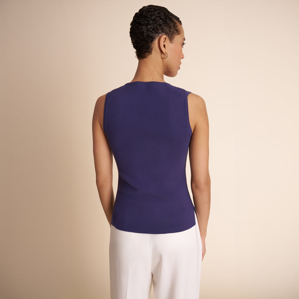 Woman wearing a sleeveless purple top and white pants on a beige background